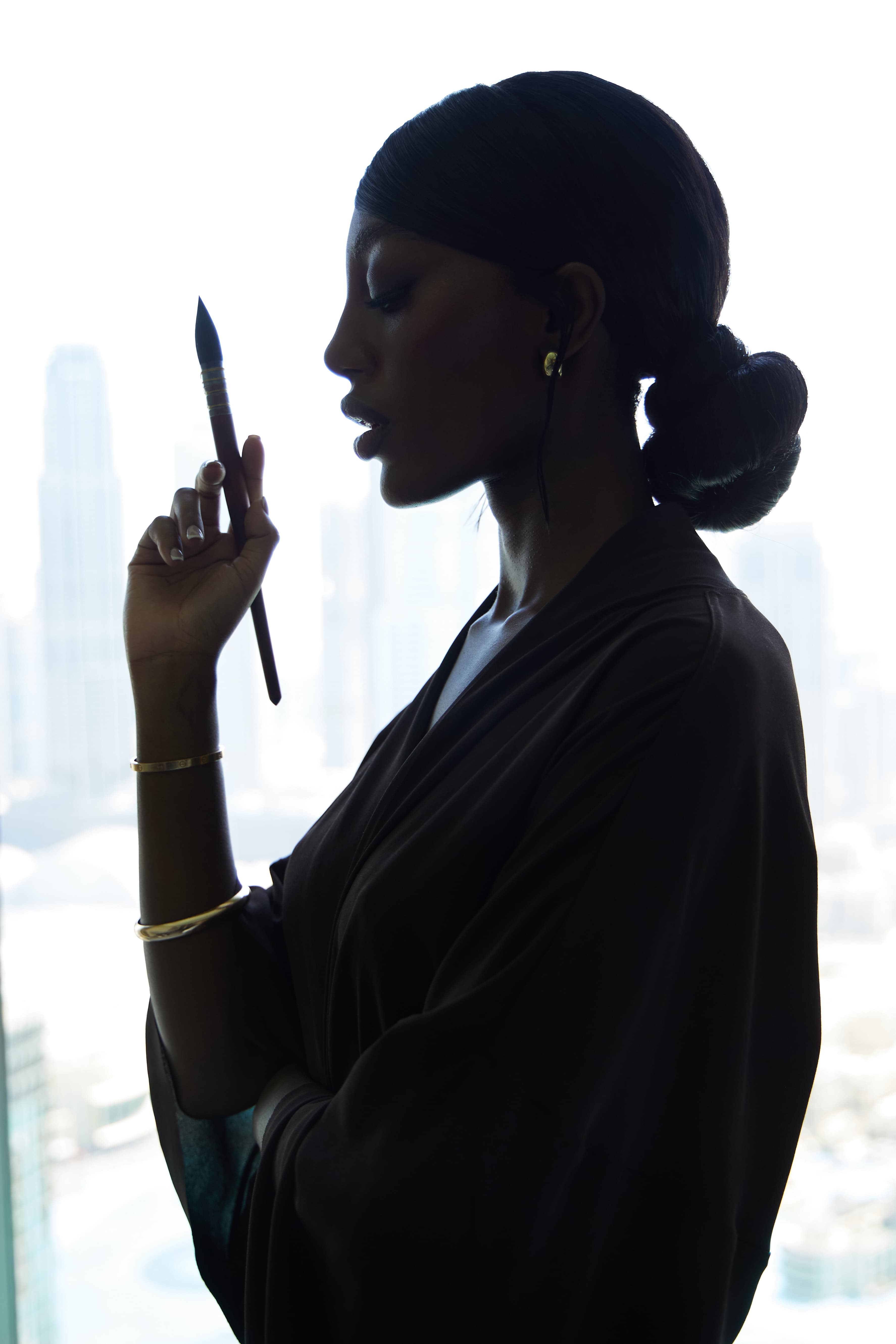 Ava Noémie holding a paintbrush, silhouetted against a window